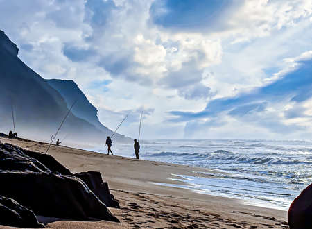 People fishing on a beach in a hazy atmosphere near sunsetの写真素材