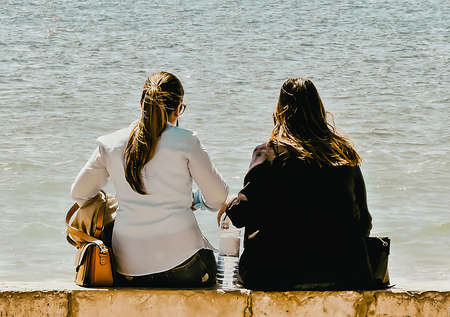 Two women on a concrete wall looking out to sea
