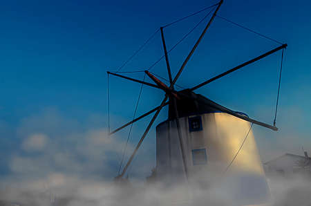An old windmill on a hill through fog and cloudsの写真素材