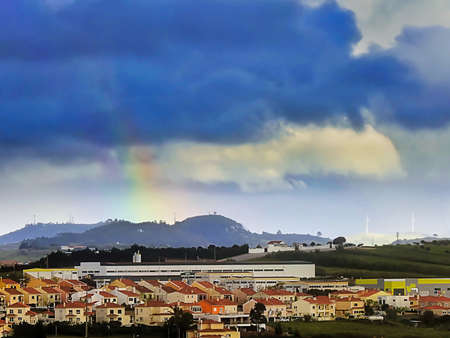 Landscape with a village in the distance and a piece of rainbow in the skyの写真素材