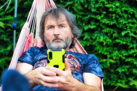 Blue-eyed man with cell phone in hands in hammockの写真素材