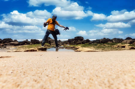 Man in orange T-shirt with camera on the shores of the Atlantic Oceanの写真素材