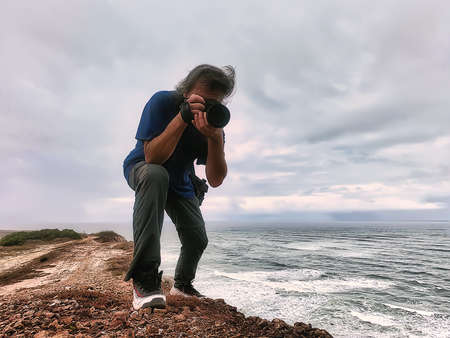 Man in blue T-shirt photographing from a rocky shore at the ocean