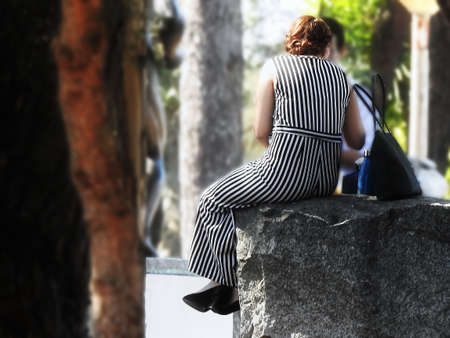 Woman in striped dress sitting on a rock in the parkの写真素材