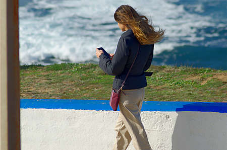 Young girl looking at cell phone by the oceanの写真素材