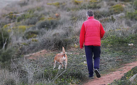 Man in red jacket walking with dog in the field