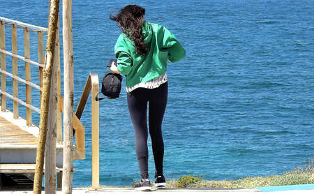 Brunette in tights with green blouse taking pictures by the ocean