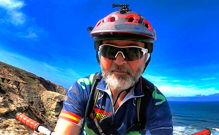 Cyclist with red helmet and blue gear pedaling near the ocean