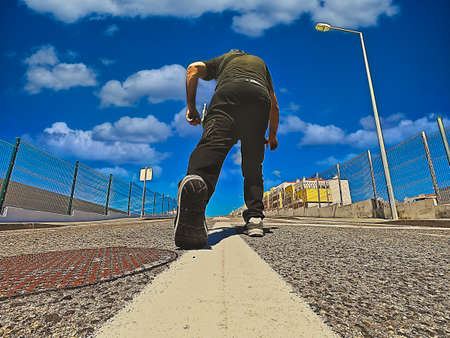 Adult man climbing a sloping street towards buildings