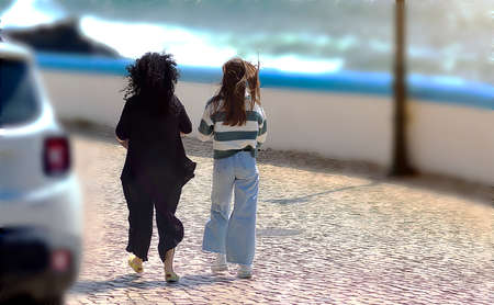 A mother with a daughter walking on the sidewalk on a windy day
