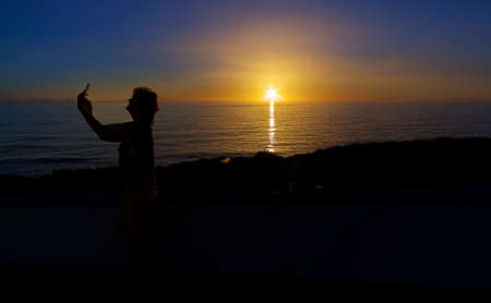 Woman taking a photo with her cell phone at sunset