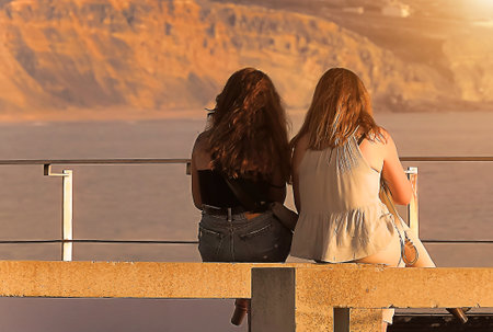 Two women standing on the bench looking at the sunsetの写真素材
