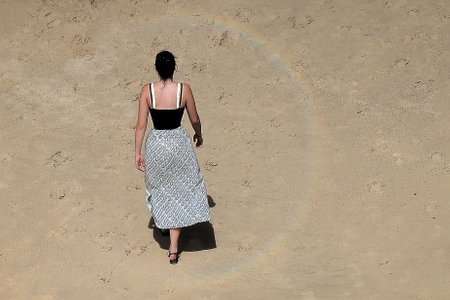 Young woman in skirt and black top walking on the beachの写真素材