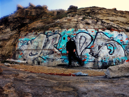 Adult man posing next to a graffiti wall on a beach