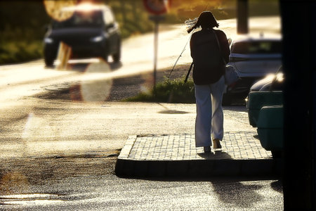 Woman walking among cars with the sun in front of herの写真素材