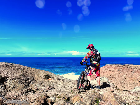 Cyclist with a red helmet pedaling by the oceanの写真素材