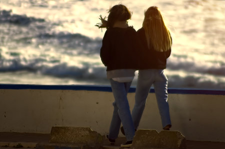 Two young women walking on the ocean shoreの写真素材
