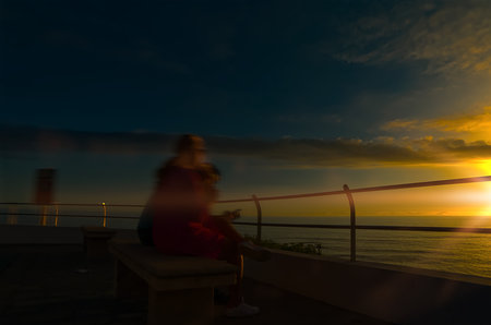 Silhouettes in motion on a bench at sunsetの写真素材