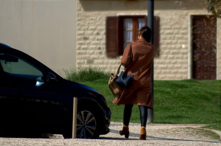 Woman with a bag on her shoulder walking on the sidewalkの写真素材