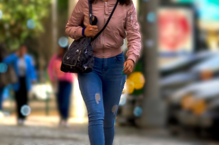 Woman with a bag on her shoulder walking on the sidewalkの写真素材