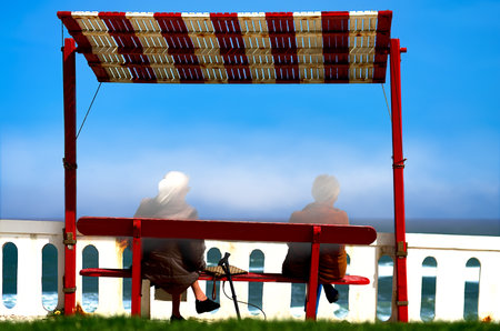 Two elderly women on a bench looking at the oceanの写真素材