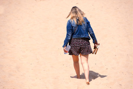 Blonde in jeans jacket walking barefoot on a beachの写真素材