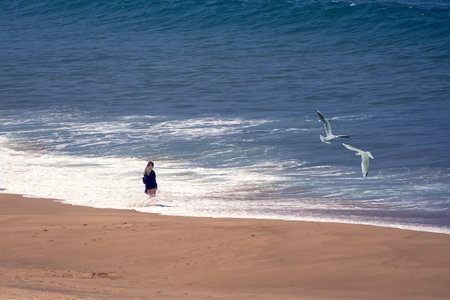 A woman with her feet in the ocean water looking into the oceanの写真素材