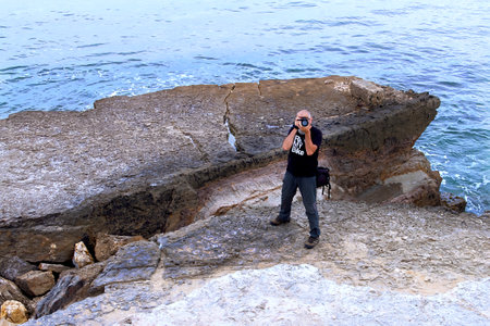 Adult man with camera taking pictures at the oceanの写真素材