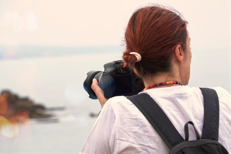 Redhead with camera and backpack on the edge of the ocean