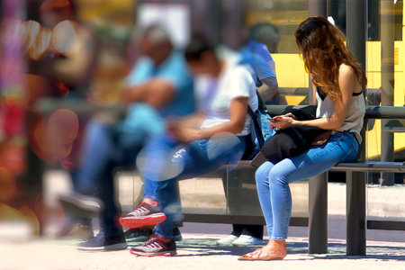 People waiting for the bus with their phones in their handsの写真素材