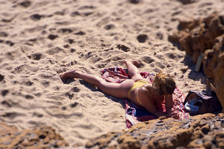 Woman in yellow bikini lying on the sand tanningの写真素材
