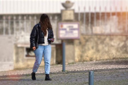 Back view of young woman in jeans and leather jacket walking on the street
