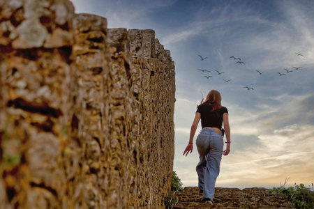 Young woman standing on the ruins of an ancient fortress with flying birds