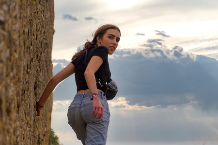 Beautiful young girl in a black T-shirt and blue jeans on the background of the skyの写真素材