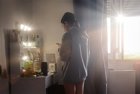 Young woman standing in front of a mirror and looking at her smartphoneの写真素材