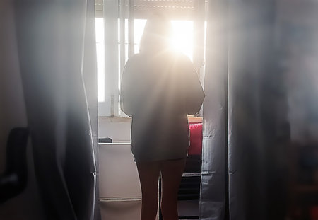 Back view of young woman standing in the toilet and looking out the windowの写真素材