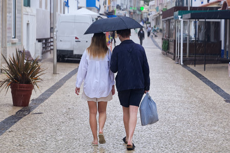 Back view of a couple walking on the street under an umbrella.の写真素材