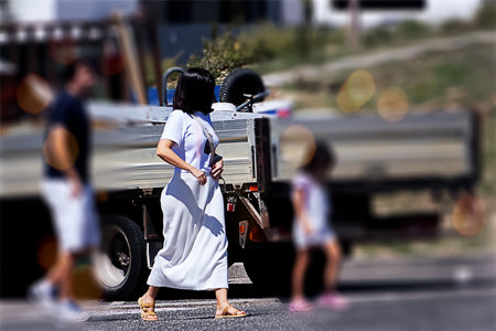 A young woman in a long white dress is walking on the road.