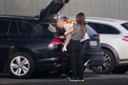 Young woman with her baby standing in front of car on streetの写真素材