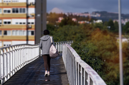 A young woman with a backpack walks along the bridge over the river.