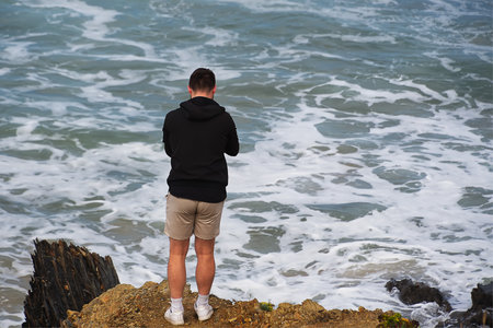 Young man standing on the edge of a cliff and looking at the seaの写真素材