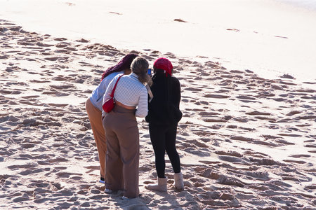 Three women standing on the beach and looking at each other. Rear view.