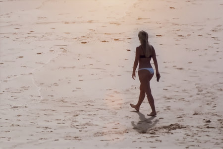 A young woman walking on the beach in the early morning light.の写真素材