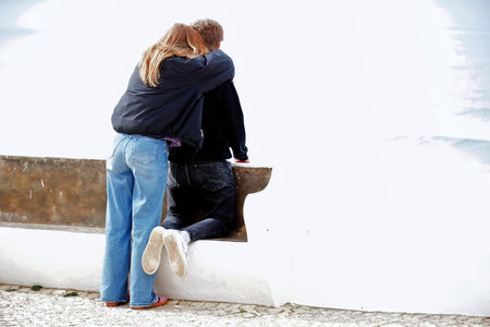Young couple sitting on a bench by the sea looking at each otherの写真素材