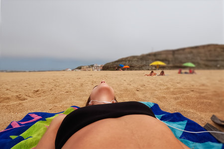 Young woman lying on the sand at the beach and sunbathingの写真素材