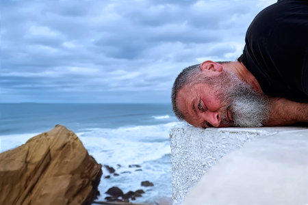 Mature man lying on the edge of a cliff and looking at the seaの写真素材