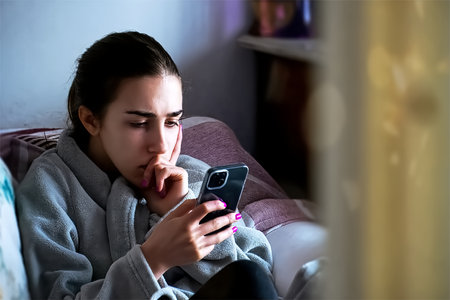 Young woman sitting in bed and using mobile phone. Close-up.
