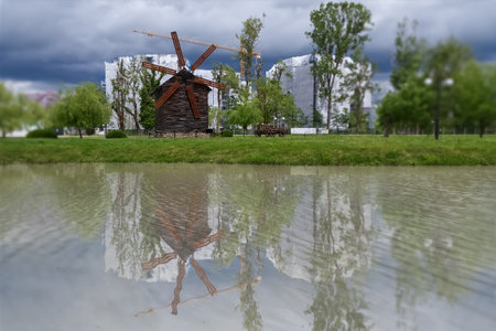 Old wooden windmill in the city park with reflection in the water