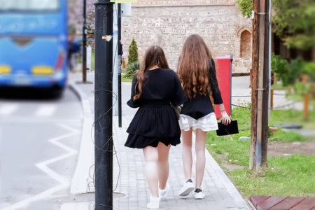 Back view of two schoolgirls walking in the street and looking at the camera
