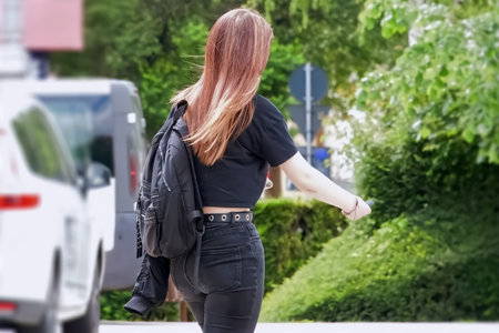 A young woman in a black T-shirt with a backpack walks along the street.